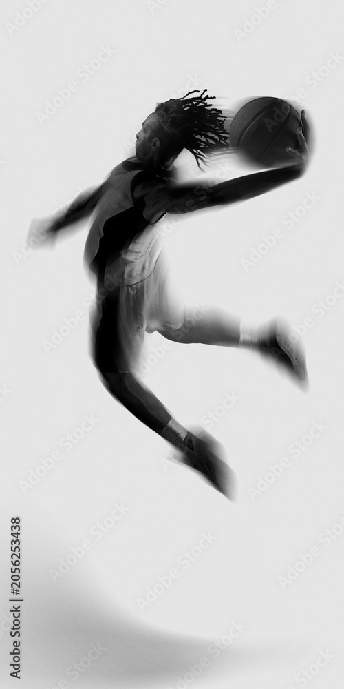 Naklejka premium Black and white basketball player flying with ball in motion blur on white background. Concept of aerial power, creative sports poster, explosive leap, and game winning drive.