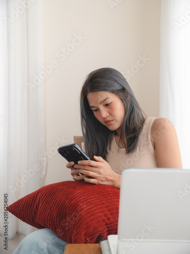 Young Asian woman texting on phone, contemplative remote student