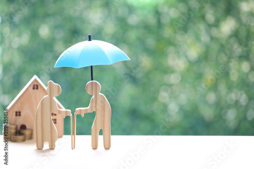 Couple wooden figures standing with a miniature house and coins, representing retirement home planning, property investment, real estate for seniors and financial security for old age
