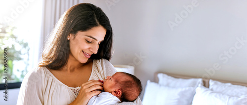 Loving Middle Eastern mother gently cradling her newborn baby in a bright bedroom, conveying warmth and maternal affection, natural light, minimalist composition with copy space.