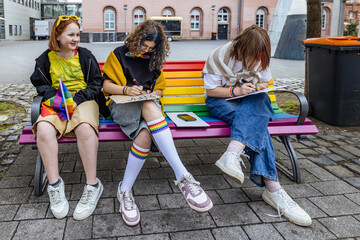 Friends preparing signs for LGBTQ pride parade on rainbow bench