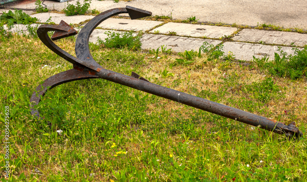 Αυτοκόλλητο Large vintage rusty iron grapnel anchor with four prongs lying on green grass near a concrete pathway