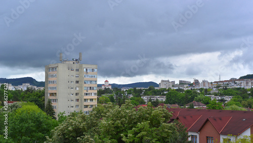 A sky filled with nimbostratus clouds, threatening a summer storm over an Eastern European city. Anti-aircraft radar antennas and a siren on a building in the foreground.