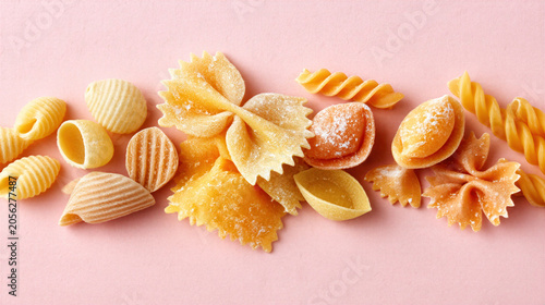Assorted dry pasta on pink background with various shapes and textures