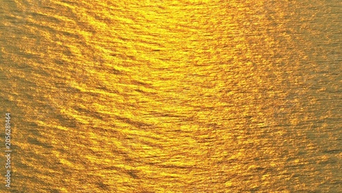 Obraz na plátně Aerial drone view capturing golden sunset reflections shimmering across ocean waves, highlighting natural light patterns, rippling textures, and tranquil marine environment from above