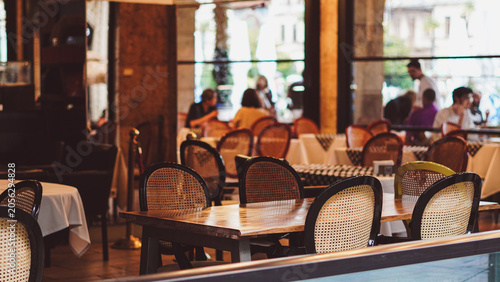 фотографія Cozy restaurant interior with empty tables and chairs near window with people