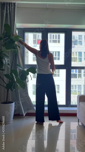 Close-up video of a woman pulling back window curtains to let natural light into a room. Lifestyle scene representing morning routine, home comfort, fresh start and everyday living.