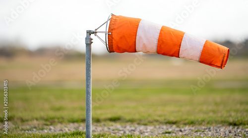 Vibrant orange and white windsock indicating wind direction on a green field, symbolizing air currents, weather patterns, and flight safety