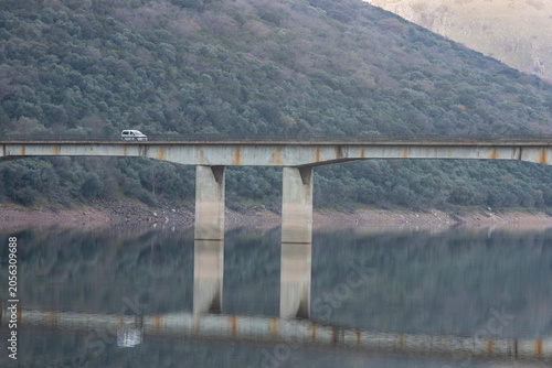 Fotografie White van crossing concrete bridge over calm lake water with reflection at Puent