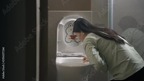 Tired young woman feeling sick and vomit into toilet bowl sitting on bathroom floor due to early stages of pregnancy or food poisoning or drinking alcohol intoxication, drunkenness, nausea, illness