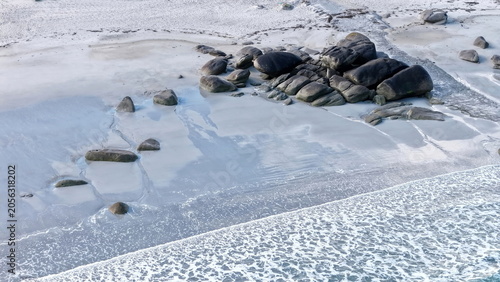 Eine beeindruckende Luftansicht vom Plage de Boutrouilles, bei der sanfte, weiße Wellenmuster auf den hellen Sandstrand und die charakteristischen, dunklen Felsformationen treffen.