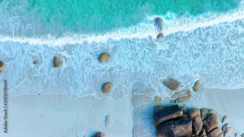 Foto Faszinierende Drohnenaufnahme vom Plage de Boutrouilles: Türkisblaues Wasser und weißer Gischt-Schaum treffen auf hellen Sandstrand und markante, dunkle Granitfelsen