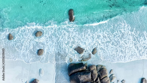 Faszinierende Drohnenaufnahme vom Plage de Boutrouilles: Türkisblaues Wasser und weißer Gischt-Schaum treffen auf hellen Sandstrand und markante, dunkle Granitfelsen.