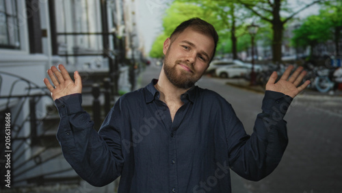 Canvas Print Man shrugging with palms up and tilted head on a cobblestone city street, wearing navy button shirt and beard; nonchalant acceptance