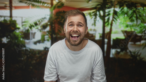 Bild auf Leinwand Man smiling with fists raised and visible face in a hotel building wearing white t shirt and beard; joy celebration success