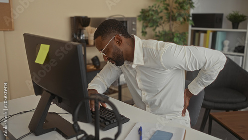 Quadro em tela Man hold lower back for backache at office while typing at desktop keyboard and looking at monitor, seated at desk with glasses; discomfort work strain
