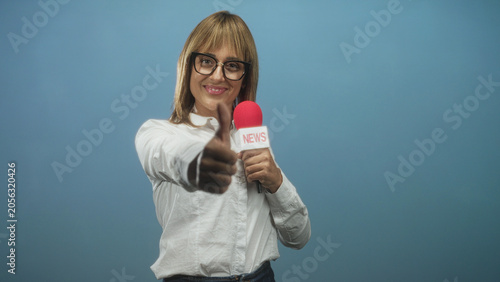 Foto Woman reporter holding red microphone labeled news gives thumbs up to camera in studio; confidence approval