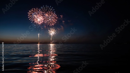 Fireworks display illuminates the dark sky over the calm water surface during a peaceful summer evening celebration.