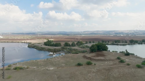 Aerial scenic view of a water reservoir and agricultural fields with high voltage power lines and electricity pylons in the background.