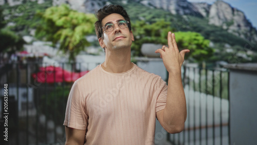 Quadro su tela Man with glasses makes finger gun gesture to temple, closed eyes and slight smile, exposed hand visible on building balcony; wry resignation