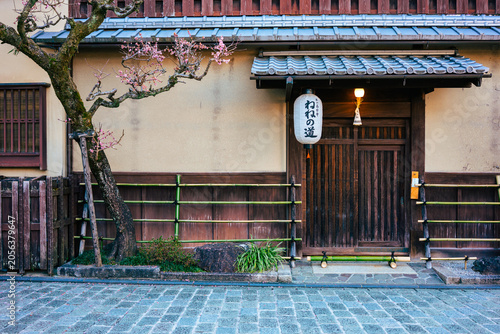 Traditional Japanese house facade with a blooming plum tree along a cobblestone street in Kyoto.