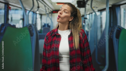 Canvastavla Woman pursing lips in a puckered mouth gesture while standing in a nearly empty bus aisle, wearing a red plaid shirt and white tshirt; urban commute contemplation