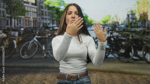Fotografi Woman flips hair and raises hands near canal street with parked bicycles and brick buildings; confidence self expression