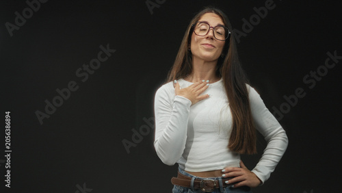 Foto Woman touching chest with hand and visible nails, wearing glasses, jeans and belt, posing against black studio backdrop; confidence pride poise
