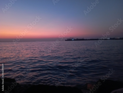 A stunning sunrise over a rustic wooden pier, featuring a vibrant sky painted in shades of orange, pink, and purple. The calm ocean waters perfectly reflect the warm gradient of the dawn, creating a p