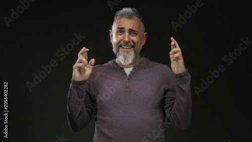 Photography Middle aged man with hands pressed together in a black studio, palms touching and pleading expression, bare hands visible; pleading apology