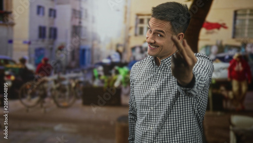 Φωτογραφία Hispanic man with moustache shows middle finger flipping gesture in street wearing plaid shirt and smiling; defiance cheeky