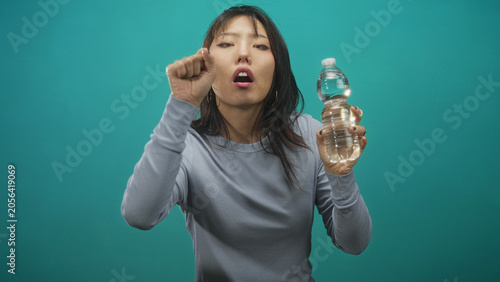 Billede på lærred Woman young chinese holding clear water bottle in right hand while raising left hand and making a startled face in studio; surprise curiosity