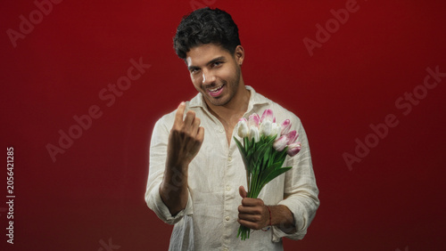 Φωτογραφία Man holding pink tulip bouquet beckons with finger in studio, wearing white shirt; flirtation offering