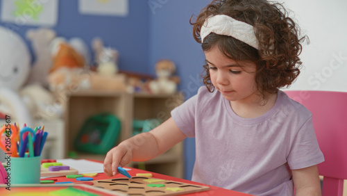 Obraz na płótnie Girl placing green wooden puzzle piece with hand on red activity table in a playroom inside a building; concentration play