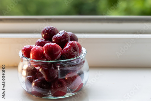 Foto Fresh sweet cherries with water droplets in a glass jar on a white windowsill wi