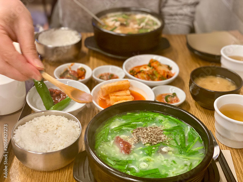 hand picking up green chili pepper with wooden spoon from korean side dish at restaurant table