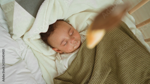 Foto Boy sleeping in cradle with olive blanket over chest, face relaxed and tiny hand visible beside mattress in building; serenity