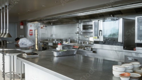 Фотография Commercial kitchen scene with shallow bokeh and soft defocused stainless steel counters and prep island, interior; background backdrop copyspace template calm