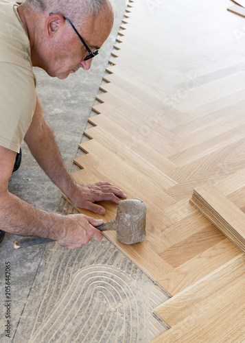 Worker installing herringbone parquet flooring with rubber mallet during hardwood floor installation