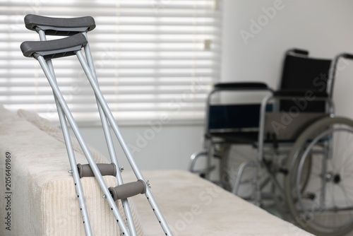 Fotografía Modern wheelchair and axillary crutches near sofa indoors