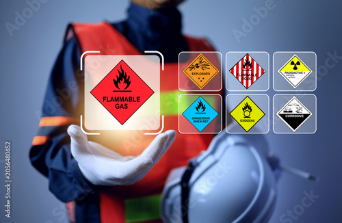 An industrial worker holds floating hazardous material placards, representing hazmat classification, dangerous goods transportation safety, and industrial safety compliance
