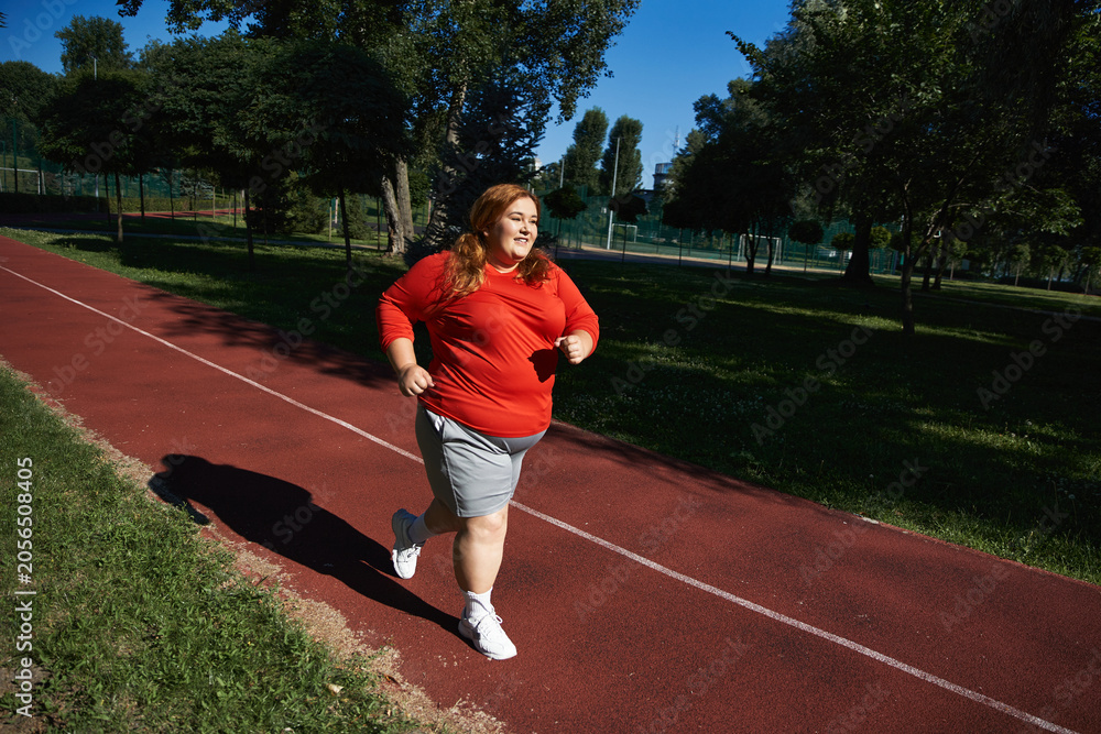 Obraz premium Empowering plus size woman enjoys outdoor running in vibrant park setting under blue skies