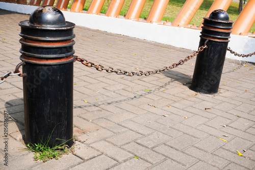 Fotografie Black bollards with chains on a paved walkway with a blurred background