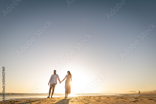 Foto Couple walking hand in hand on the beach during sunset close to the horizon