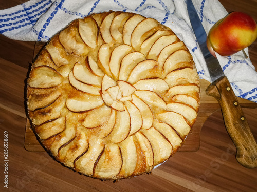Altdeutscher Apfelkuchen auf einem Holzbrett mit einem Apel und einem Kuchenmesser