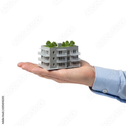 Detailed architectural model of a modern apartment complex held in a human palm wearing a blue dress shirt against a white background, real estate investment theme