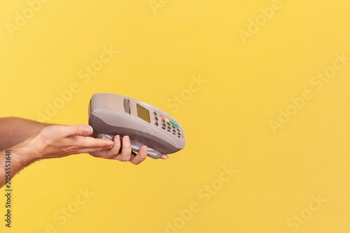 Anonymous worker holding payment terminal for contactless checkout to process secure bank transaction or mobile purchase using nfc technology isolated over yellow background with copy space