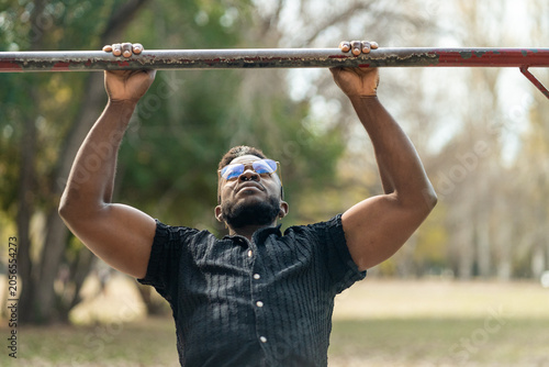 Muscular Black man doing pull-ups outdoors, focusing on fitness and strength