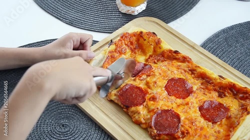 Freshly baked Roman style rectangular pizza being sliced with a pizza cutter on a wooden board.