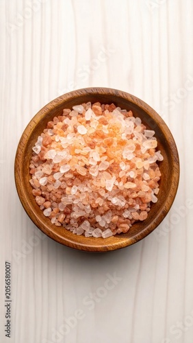 Top view of pink Himalayan salt crystals in a small wooden bowl on a light wooden background, healthy natural minerals for cooking and wellness
